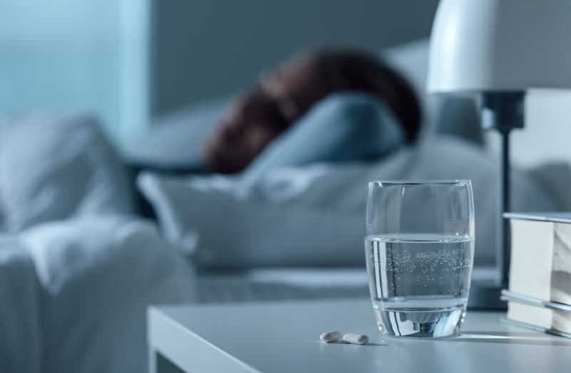 A glass of water and a zopiclone tablet on a bedside table