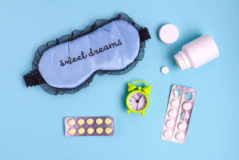 A sleeping eye mask, sleeping pills and an alarm clock laid out next to each other