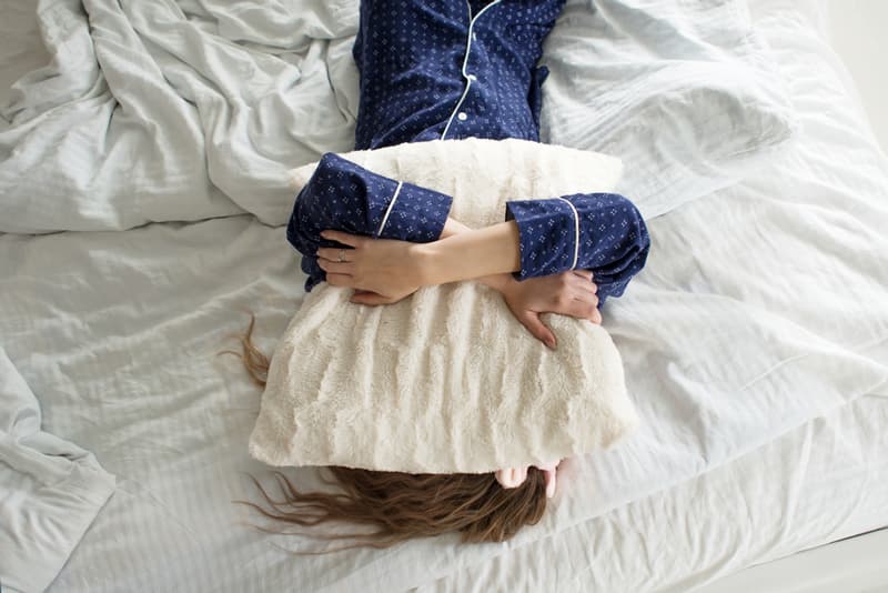 A female student suffering from a hangover and covering her face with a pillow