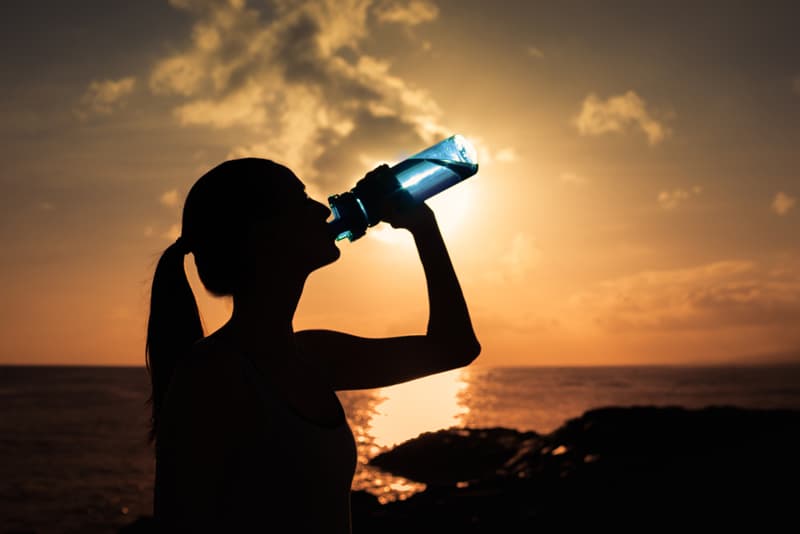 A lady drinking water from a bottle on a hot day
