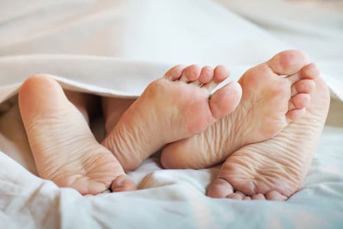 Two people's feet under the covers of a bed