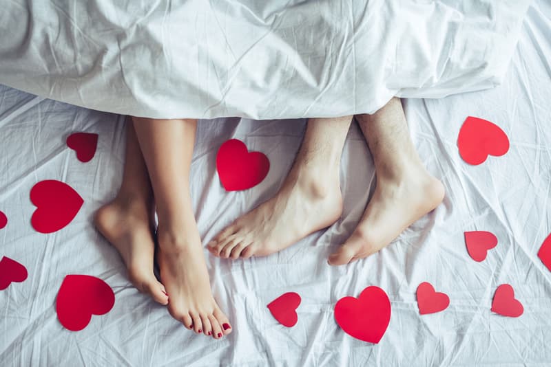 A pair of feet under the covers with love heart decorations spread around them