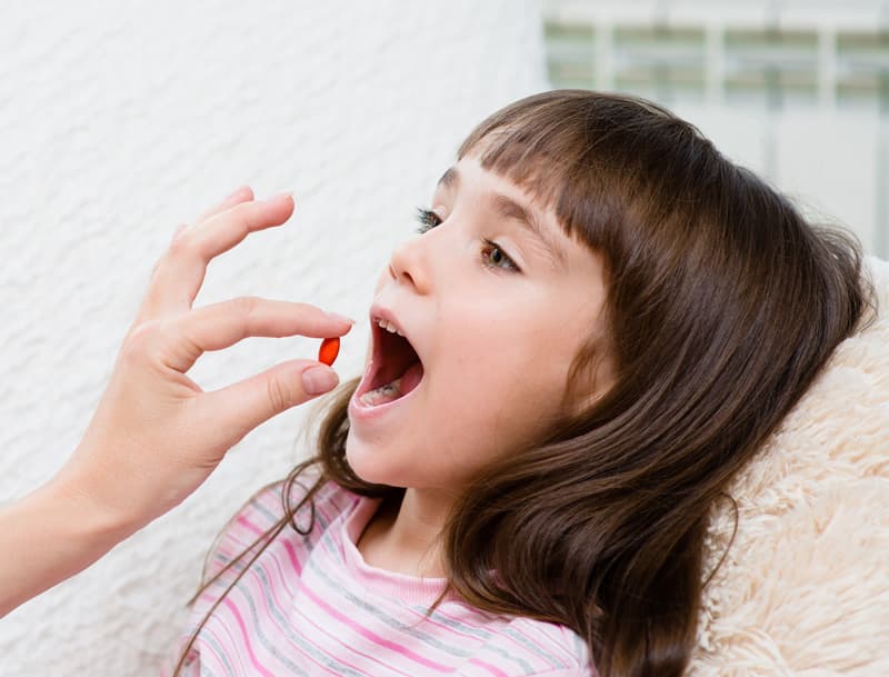 A little girl taking a Vermox tablet