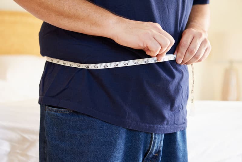 A man measuring his waistline with a tape measure