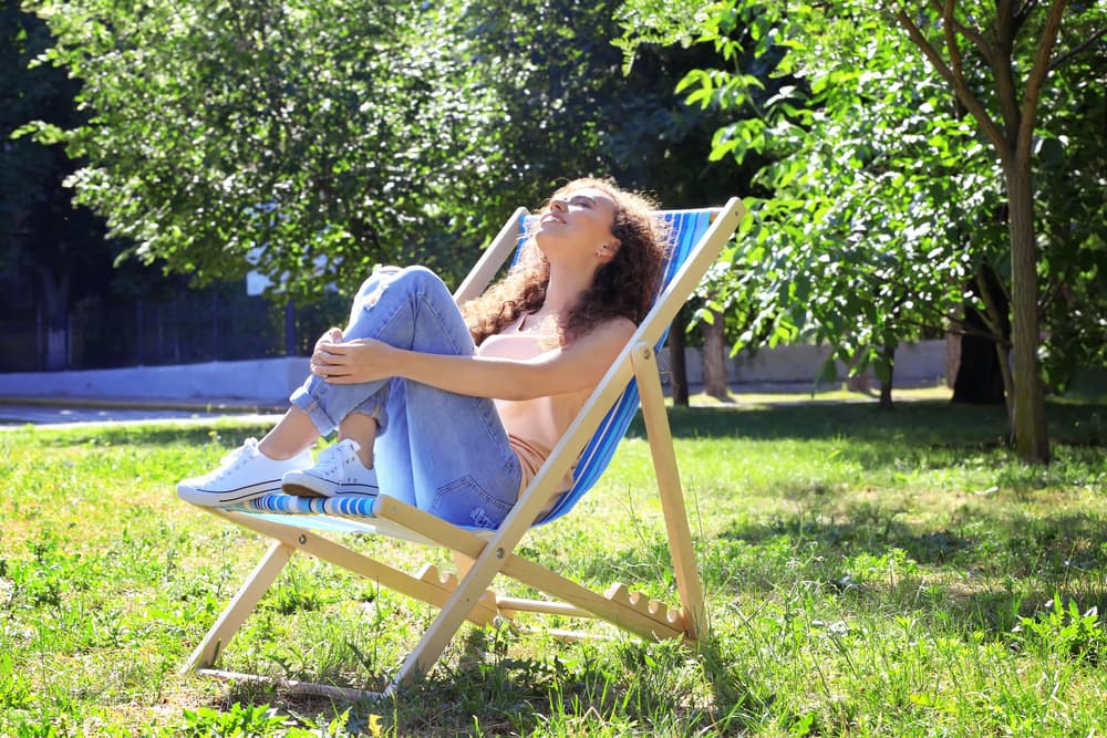 A lady sat on a deck chair in the garden on a sunny day
