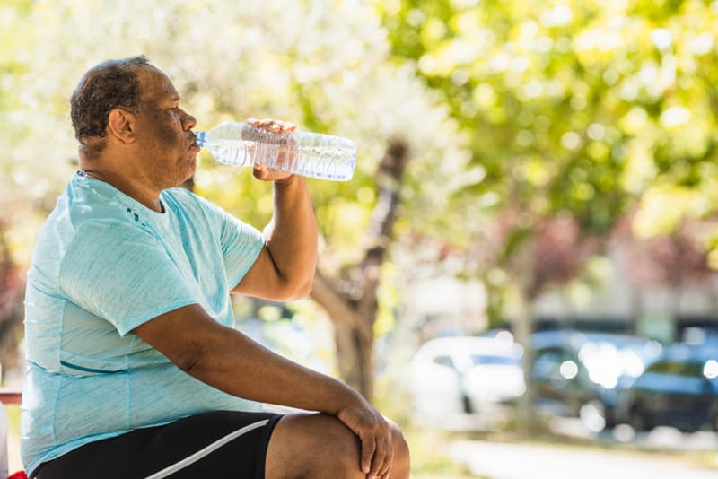 A overweight man sat on a bench drinking water