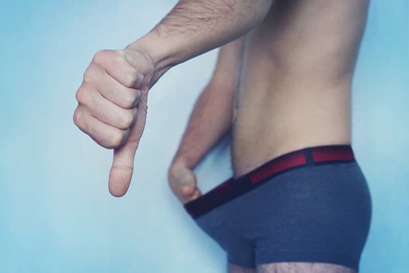 A man with his thumbs down and stretching out his boxers to look down at his penis
