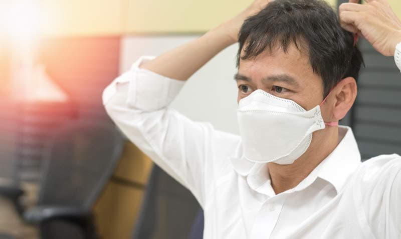 A man wearing a face mask with her hands on her head
