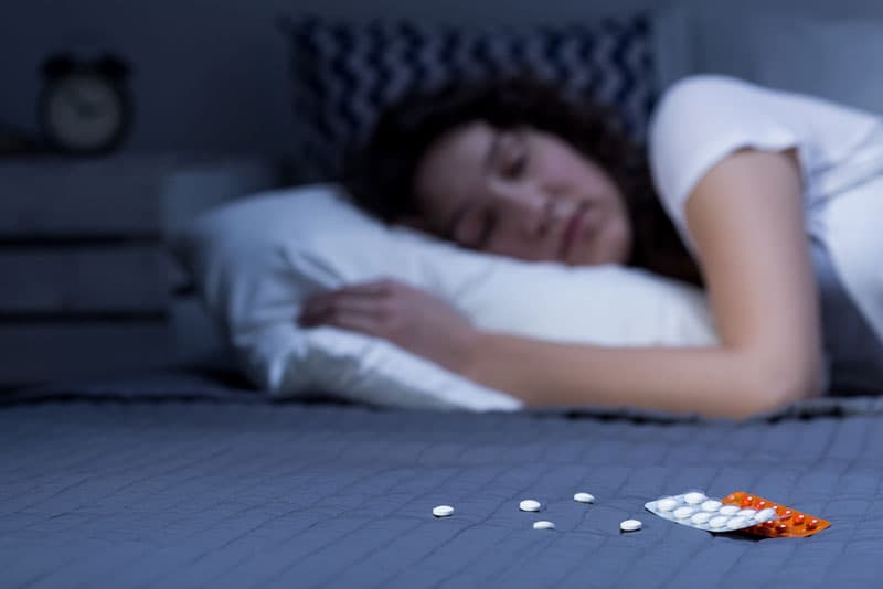 Sleeping pills laid out in front of a lady who is sleeping