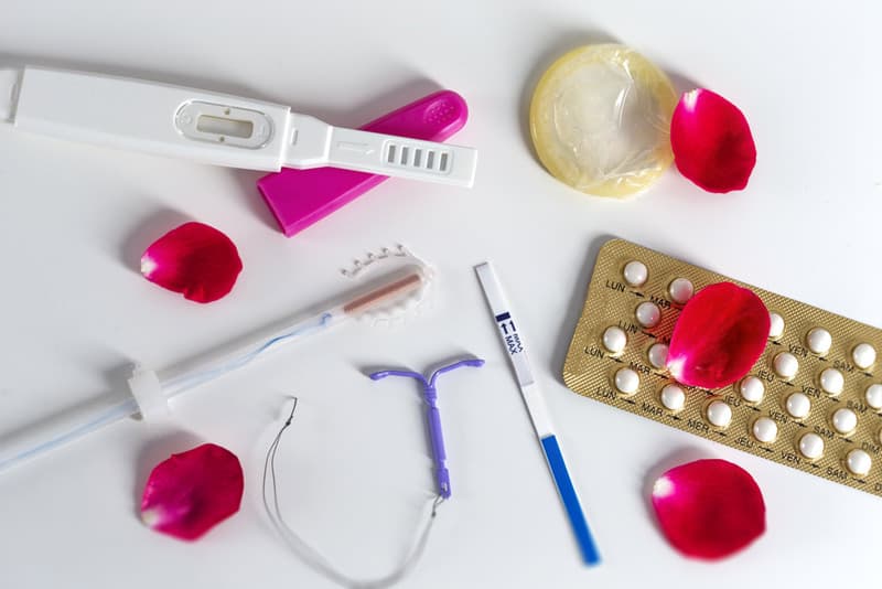 Various forms of contraception laid out next to each other with rose petals spread between them