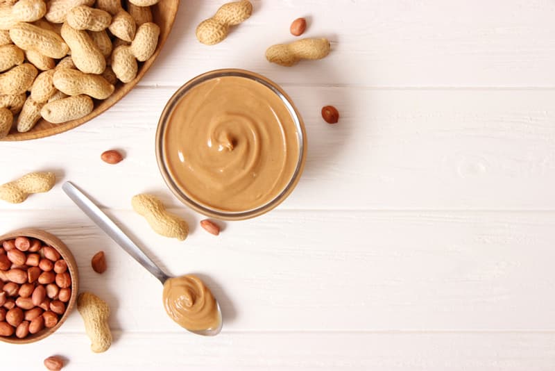 Peanut butter surrounded by various loose peanuts