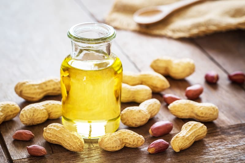 A jar of peanut oil with loose peanuts scattered around it