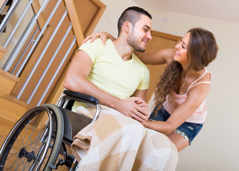 A man in a wheelchair staring lovingly into his female partner's eyes as she hugs him