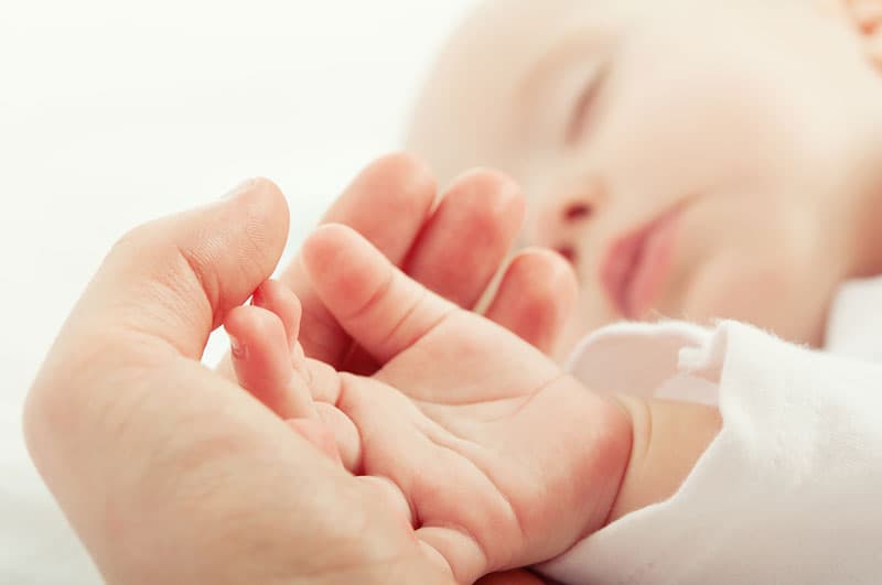 A baby sleeping with it's hand being held by an adult hand