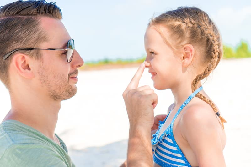 A man touching his young daughter on the nose whilst they are on the beach
