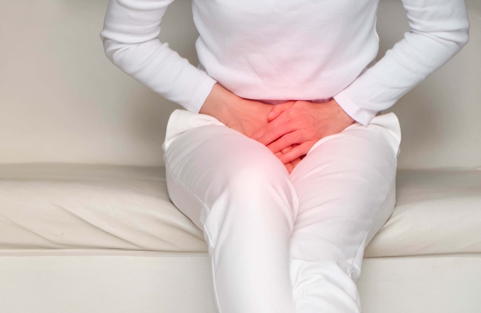 A lady sat on a sofa covering her crotch due to suffering from incontinence