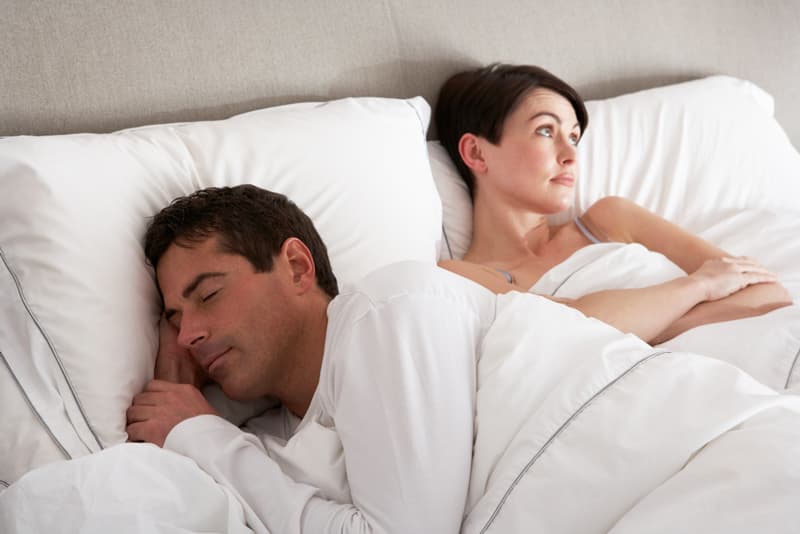 A man sleeping in bed whilst his female partner is awake and looking on wishfully
