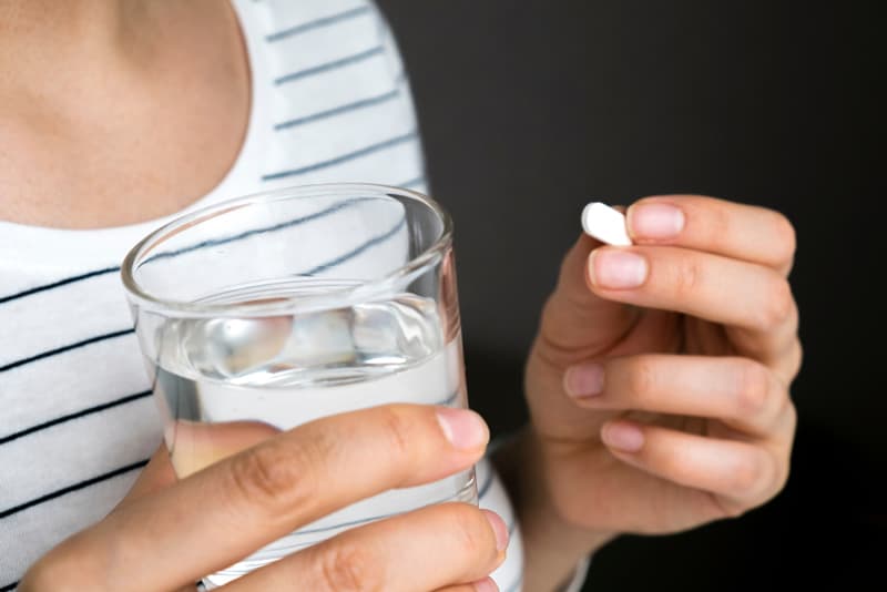 A hand holding up a glass of water and a tablet