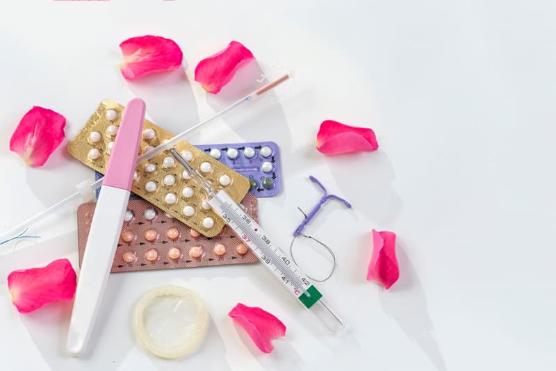 Various methods of contraception spread out over each other along with rose petals