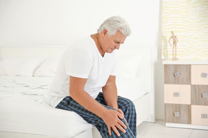 An old man sat on his bed experiencing knee pain
