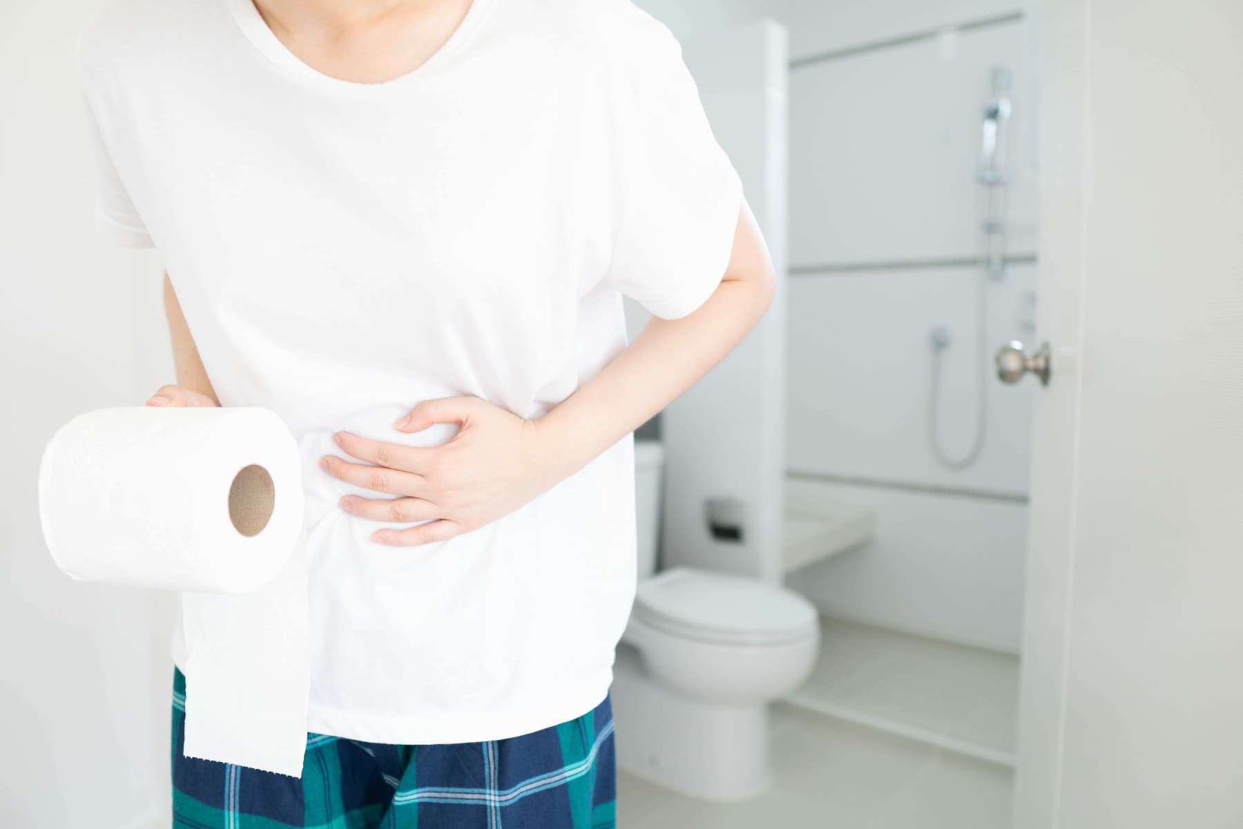 Man holding his stomach in the bathroom and a toilet roll in the other hand