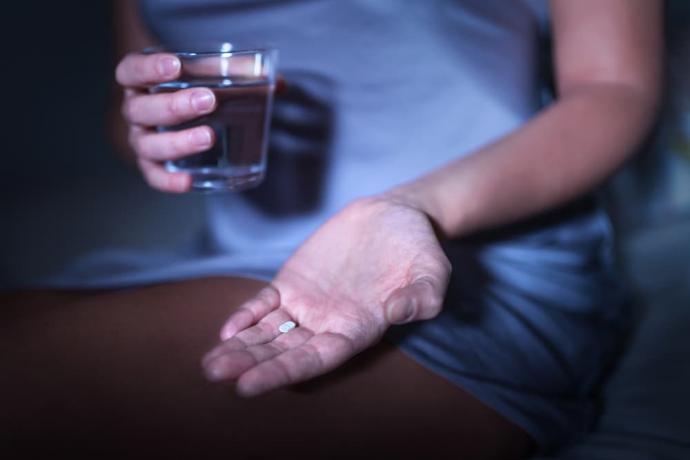 A person holding a glass of water and a tablet of Zolpidem