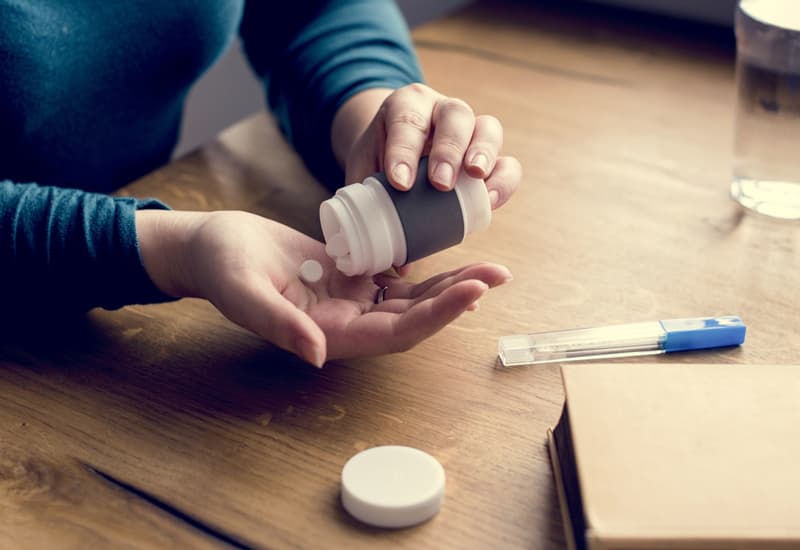 Painkiller medication being poured into the palm of a hand.