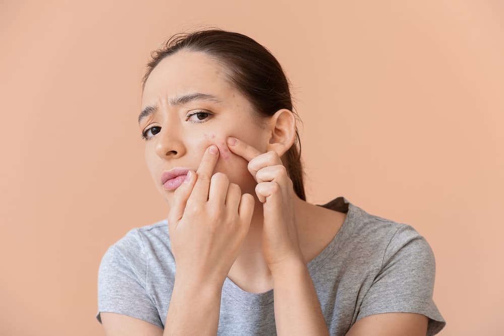 A lady assessing her facial acne in the mirror