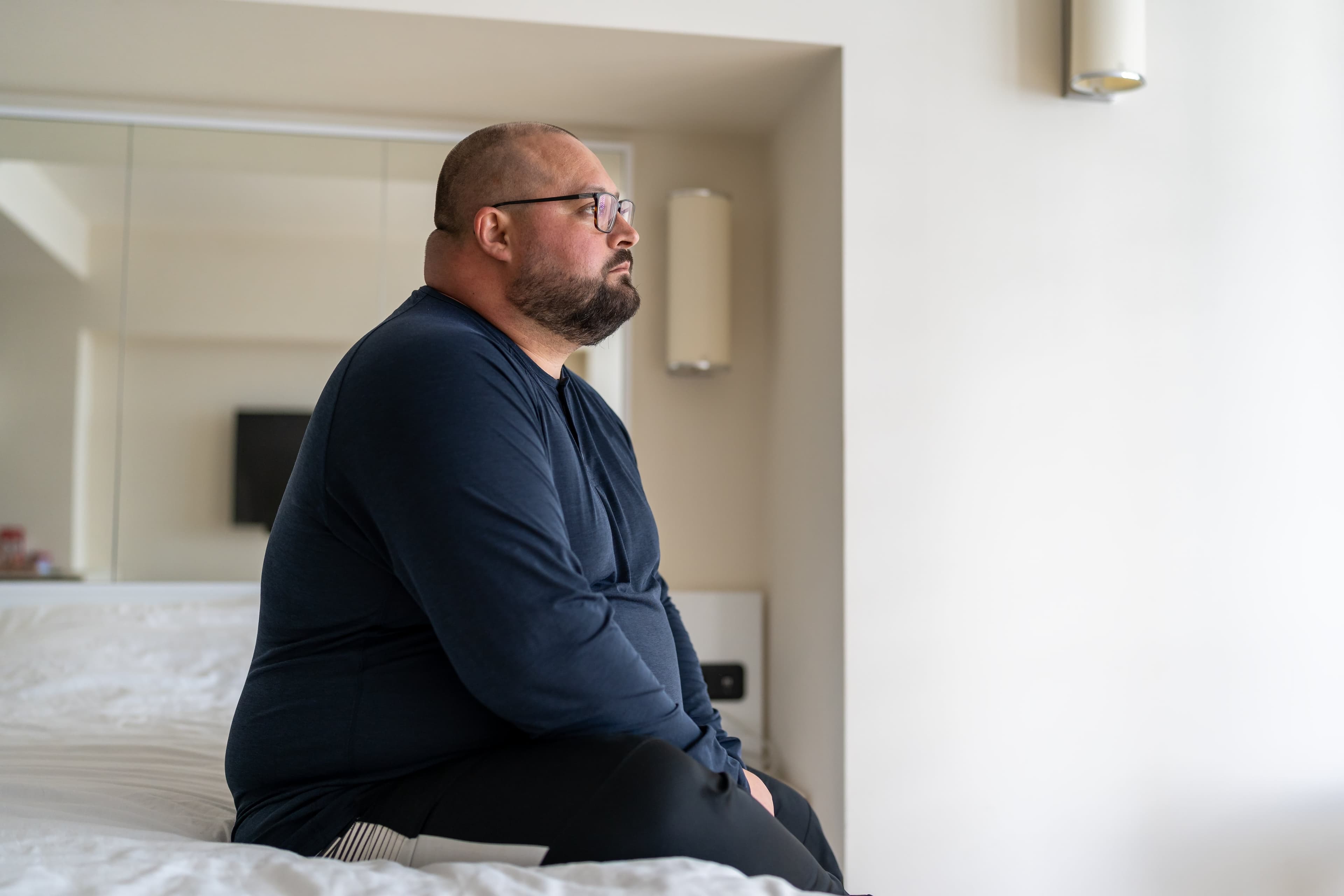 An unemployed obese British man sat on his bed gazing disappointedly out of his bedroom window. He is the ideal candidate for the UK Government's unemployed weight loss jabs trial.