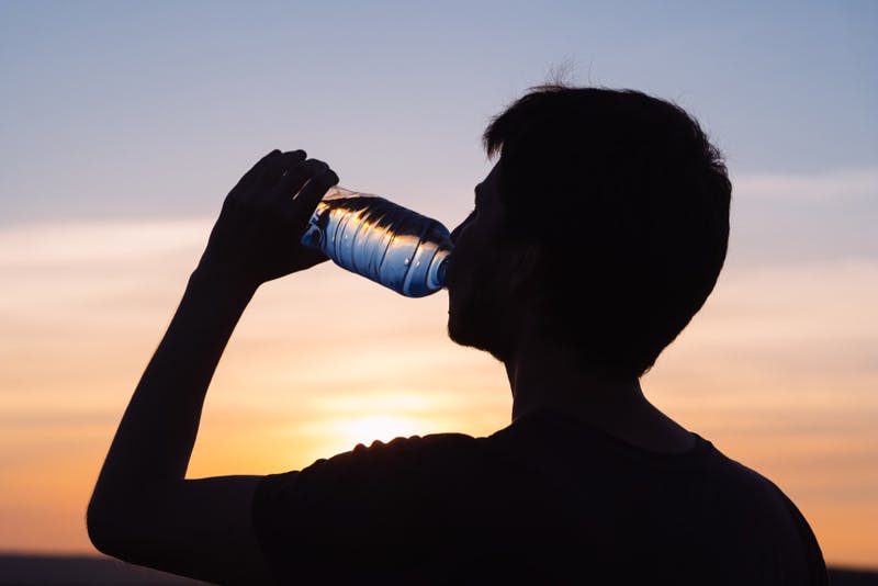Sillouette of a man drinking a bottle of water with the sun shining in the background