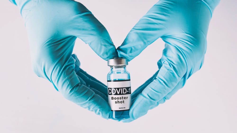 COVID booster vaccine being held by hands with rubber gloves on them