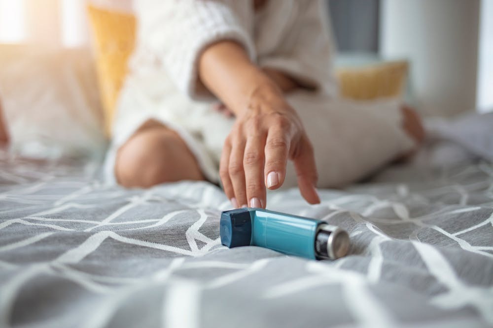 Ventolin Inhaler on a bed with someone reaching out to pick it up